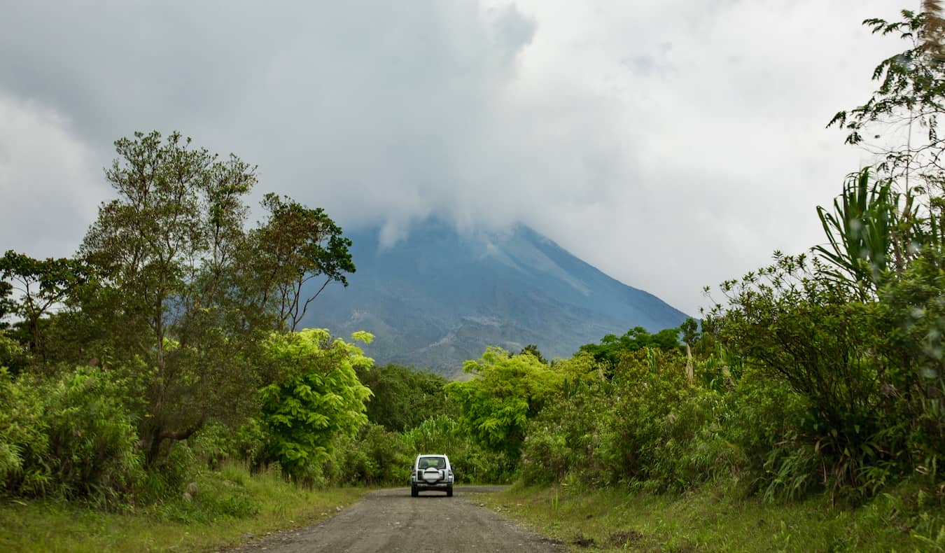 An car driving down a dirt road towards a volcano covered in clouds in Costa Rica